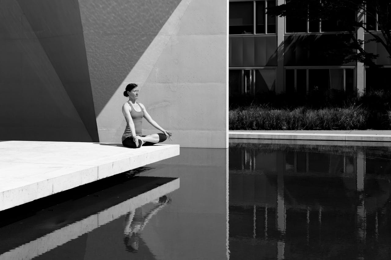 Home A woman meditating by a poolside, reflecting tranquility and focus in a minimalist setting.