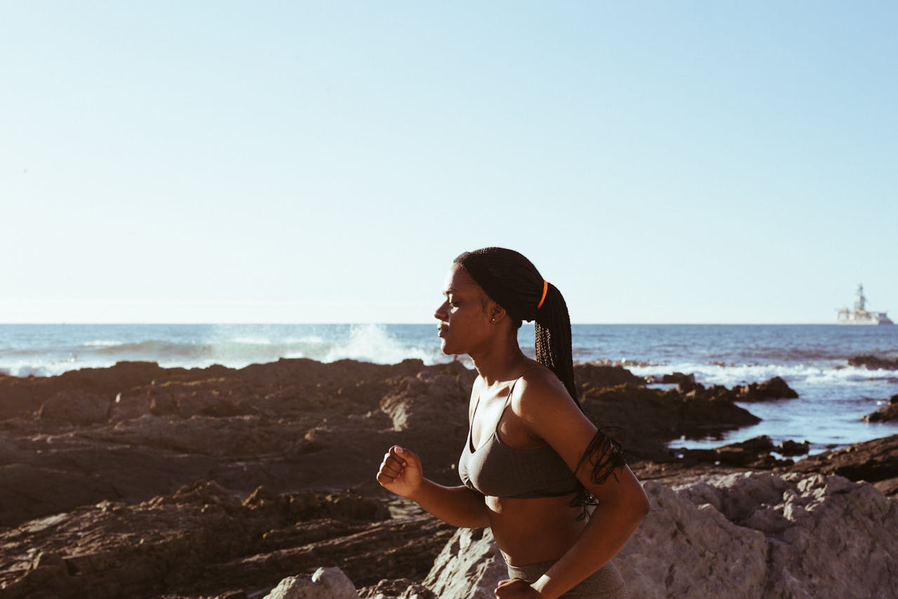 Fit woman running by the ocean, embodying health and wellness outdoors.