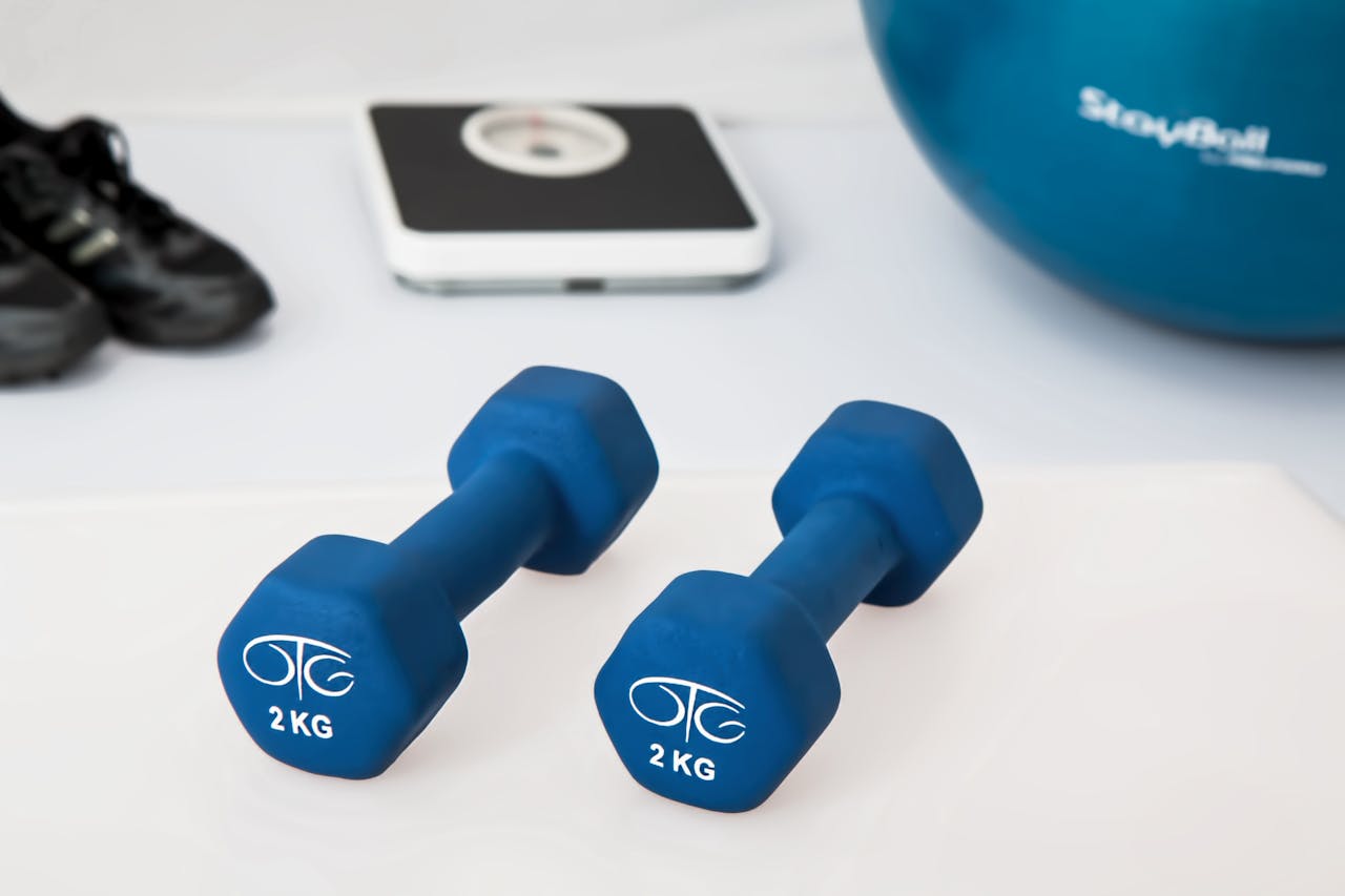 Home Blue dumbbells placed on a white surface with fitness equipment in the background.